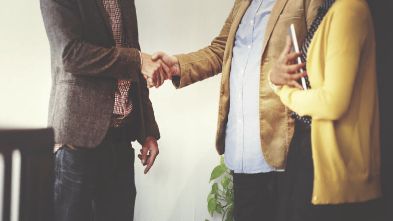 3 professional speaking together, two shaking hands.