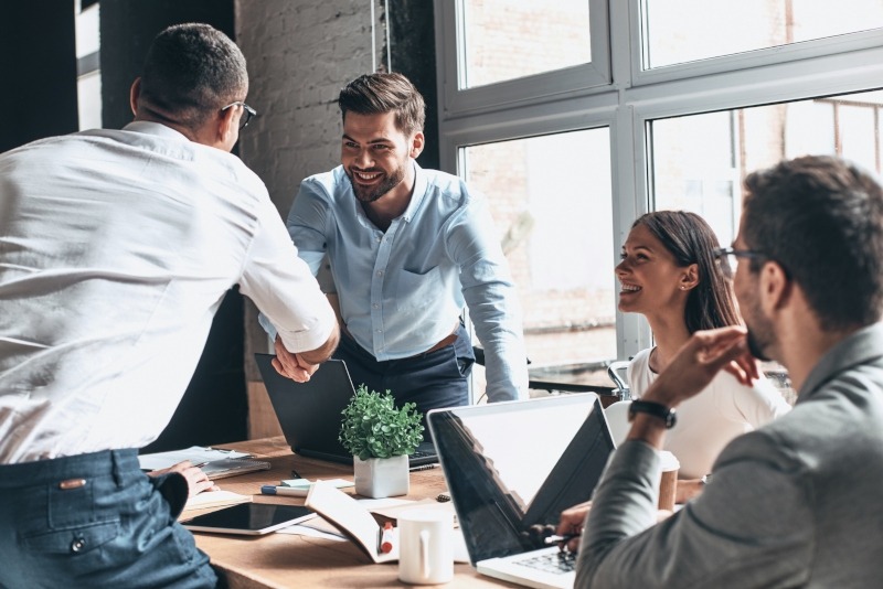 Young modern professionals in smart casual wear shaking hands and smiling while working in the creative office